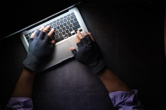 Person typing on laptop while wearing gloves